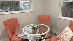 Un comedor con una mesa de vidrio rodeada por cuatro sillas naranjas y una silla de mimbre blanca.