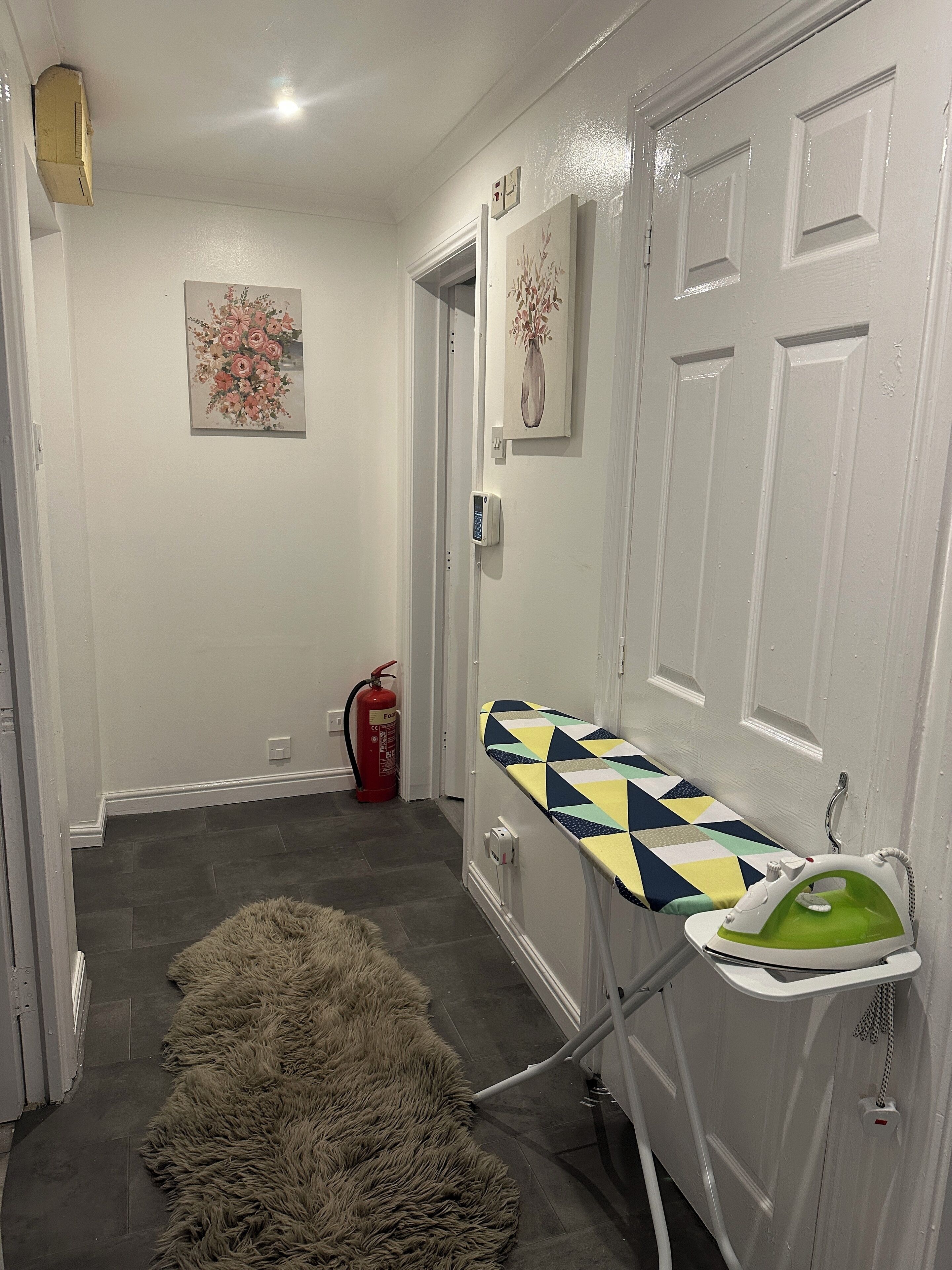 A hallway with a fur rug, a fire extinguisher, and an ironing board with an iron.