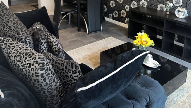 A living room with a black sofa, leopard print cushions, a coffee table, and a TV stand. There is a dining area with a table and chairs in the background. - Charming 2-bedroom flat in superb London with WiFi, AC, toiletries, quite area (London)