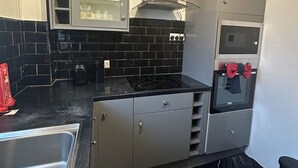 A compact kitchen with a black tiled backsplash, stainless steel appliances, and a microwave with a red bow tie. - Charming 2-bedroom flat in superb London with WiFi, AC, toiletries, quite area (London)