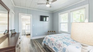 A bedroom with a bed, a ceiling fan, a TV, and a window with blinds. - Cozy Bungalow near Downtown Pensacola: Game Room, Patio + Fire Pit, 3 Bedroom! (Pensacola)