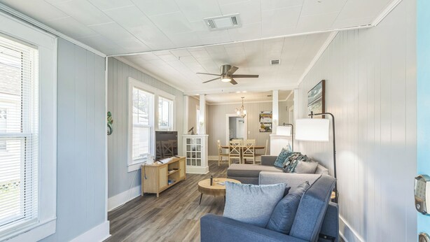 A spacious living room with a blue sofa, wooden coffee table, and a ceiling fan. - Cozy Bungalow near Downtown Pensacola: Game Room, Patio + Fire Pit, 3 Bedroom! (Pensacola)
