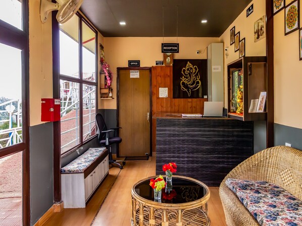 Een ontvangstruimte met een receptiebalie, een afrekenruimte, een zithoek met een bankje en een stoel, en een muur met ingelijste kunstwerken.