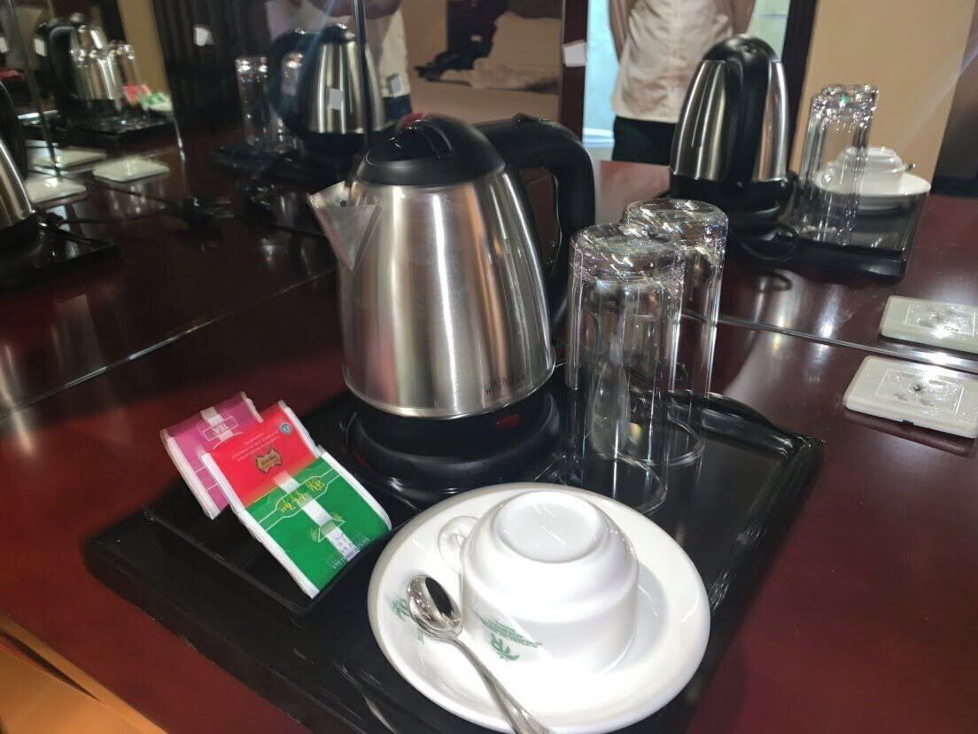 A hotel room's breakfast setup with a kettle, teacups, glasses, and tea packets.