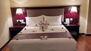 A hotel room with a large bed, two bedside tables with lamps, and a dark patterned rug.