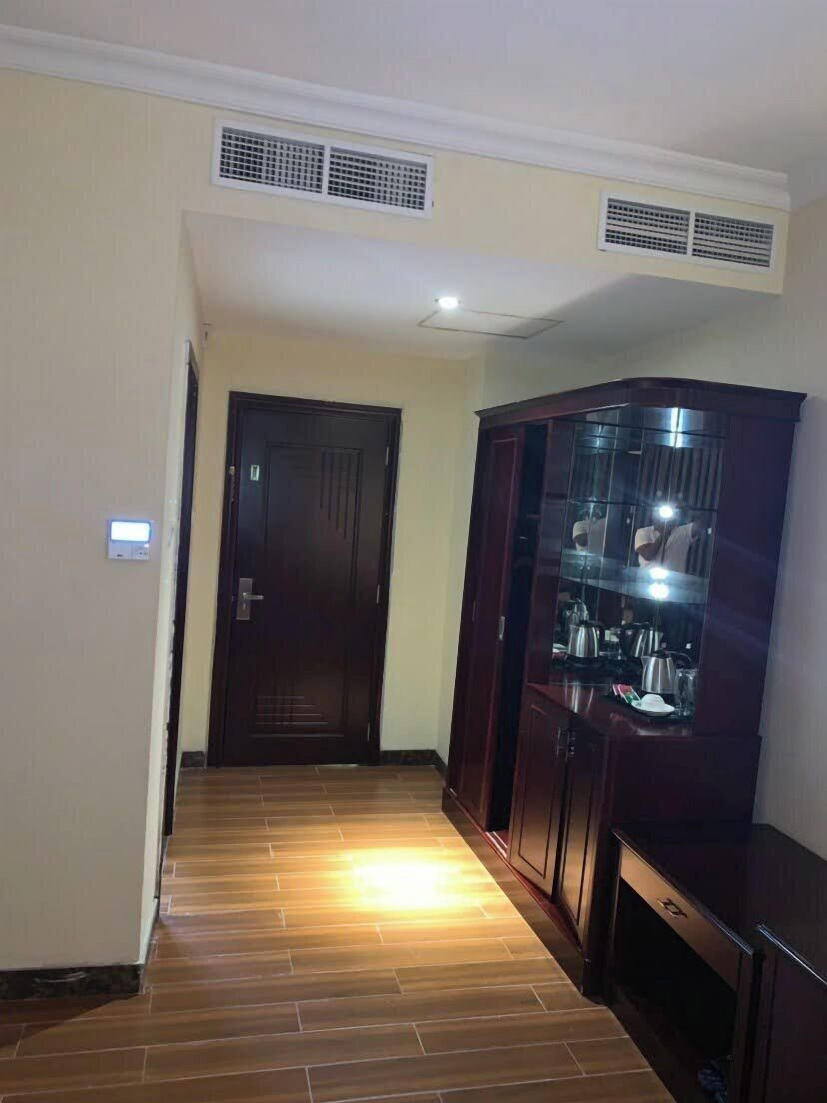 A hallway with wooden flooring, a dark wooden door, and a glass-fronted cabinet with kitchen items.