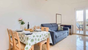 A dining area with a table set for two, a sofa, and a small table with a vase of flowers.