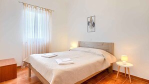 Een opgemaakt bed met een witte spreidek en kussens, een bedlampje en een klein houten nachtkastje.