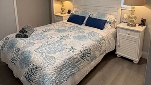 A bedroom with a bed, nightstands, a ceiling fan, a window with blinds, and a door leading to a closet. - Turtle Cove | Steps from the Beach 2BR w/Hockey/Ping-pong/Pool Table (Cocoa Beach)