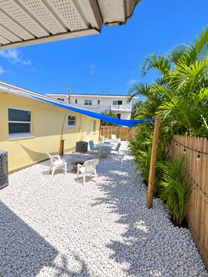 Un patio con mobiliario exterior, cerca de madera y un edificio al fondo.