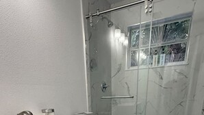 A modern bathroom with a shower, toilet, and vanity. - Turtle Cove | Steps from the Beach 2BR w/Hockey/Ping-pong/Pool Table (Cocoa Beach)