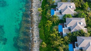 An aerial view of a coastal resort with multiple bungalow-style buildings, a rocky shoreline, and lush greenery.