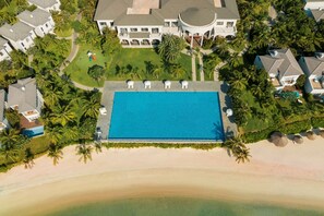 An aerial view of a resort with a large swimming pool, a beach, and a clubhouse.