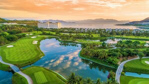 A golf course with a large building in the background, surrounded by water and greenery.