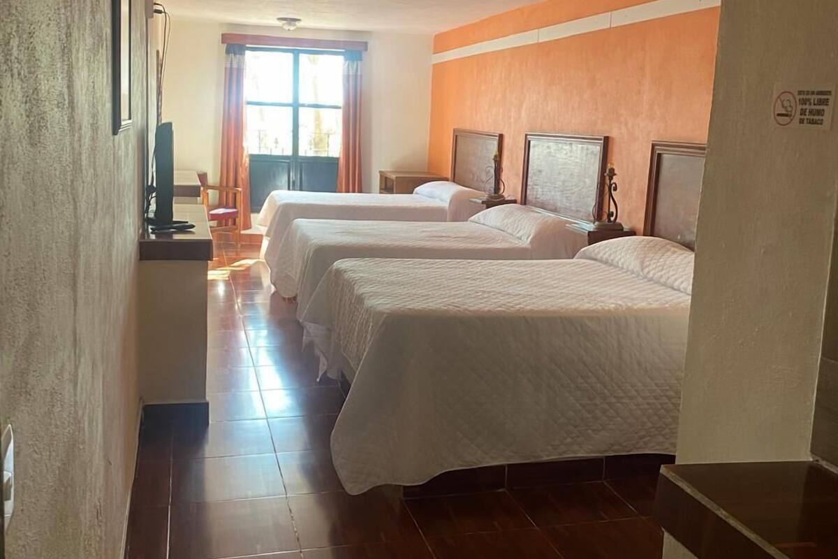 A hotel room with two beds, a television, a window with curtains, and a tiled floor.