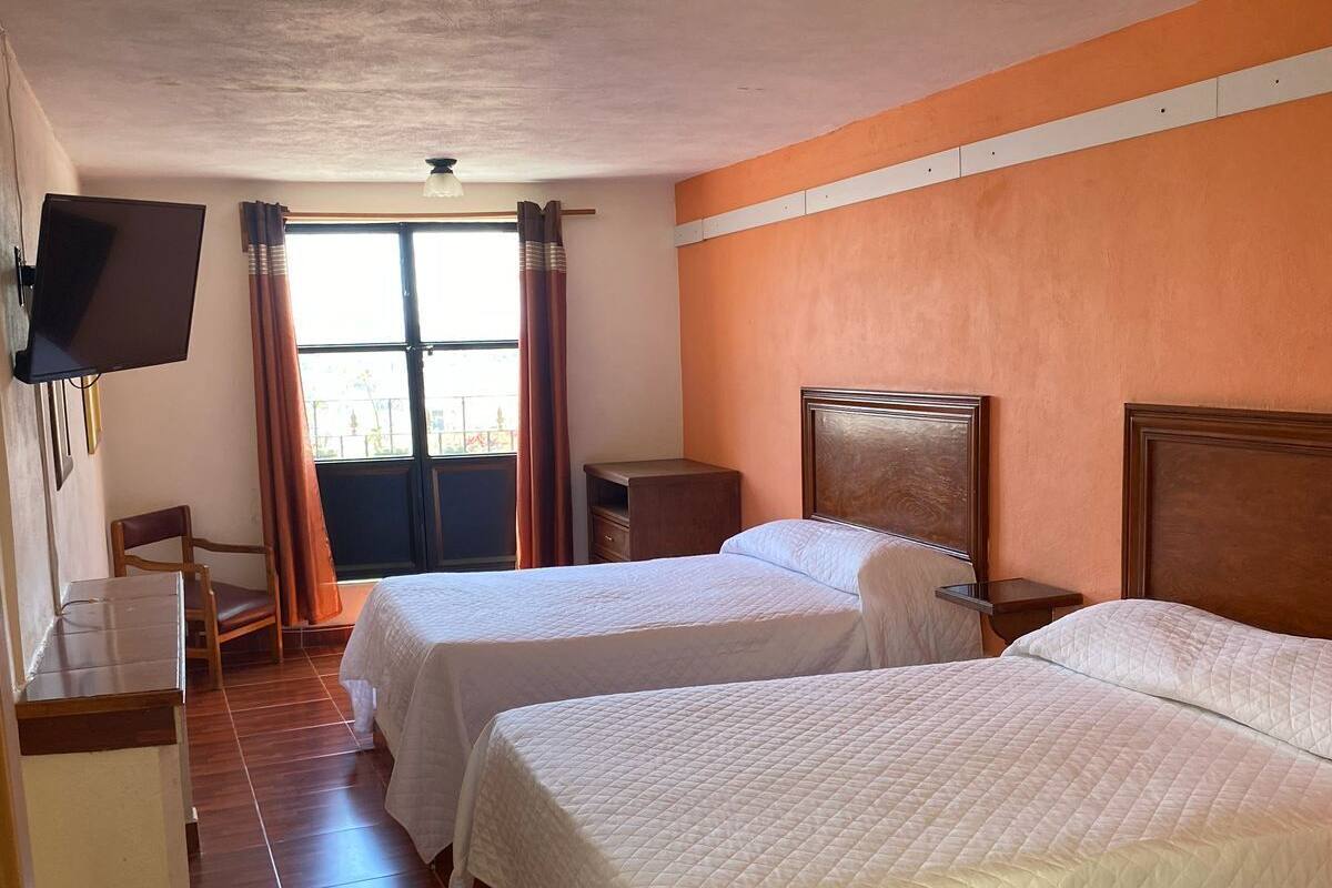 A hotel room with two beds, a TV, a desk, and a window with curtains.