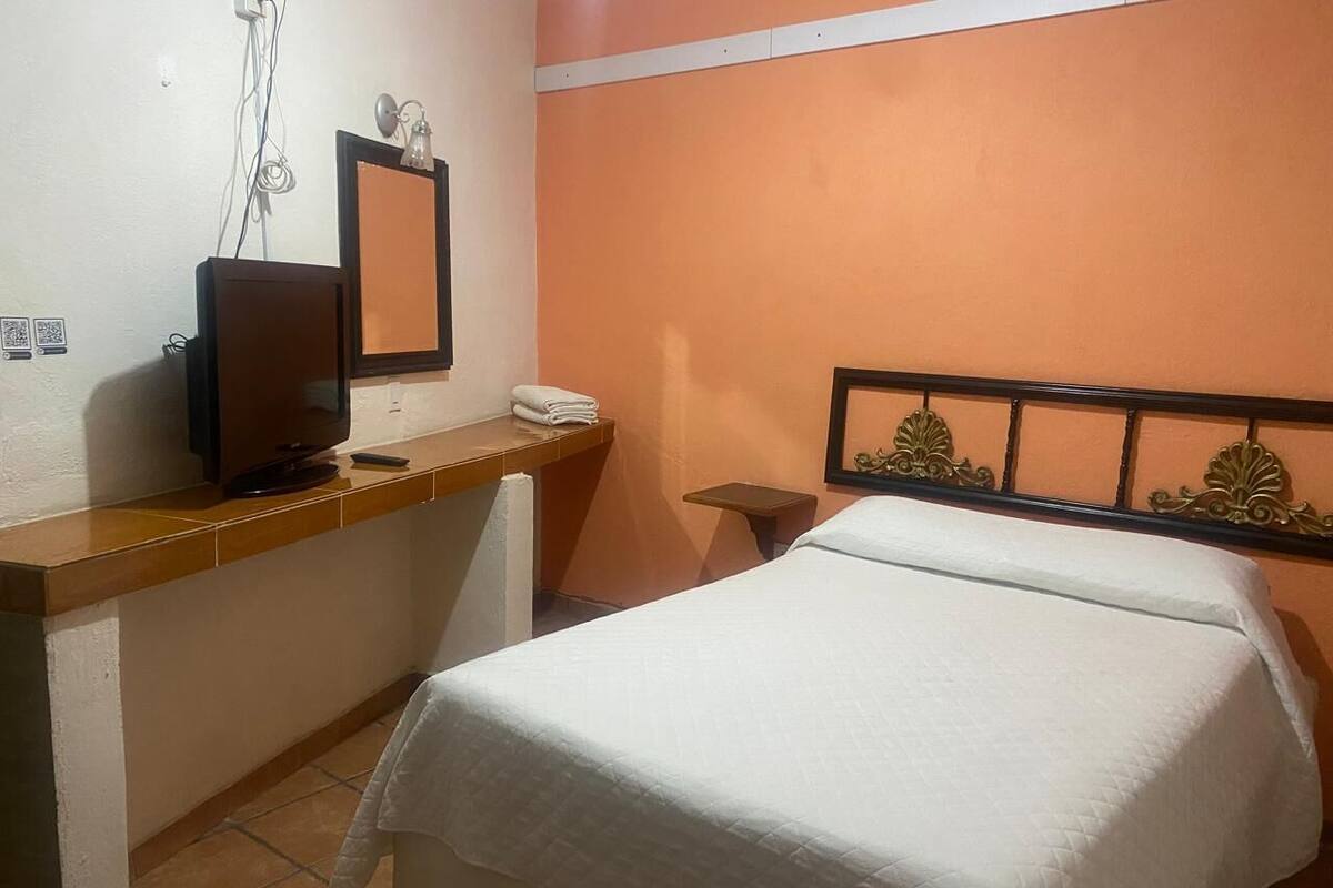 A hotel room with a bed, a desk with a computer, a small table, and a wall-mounted mirror.