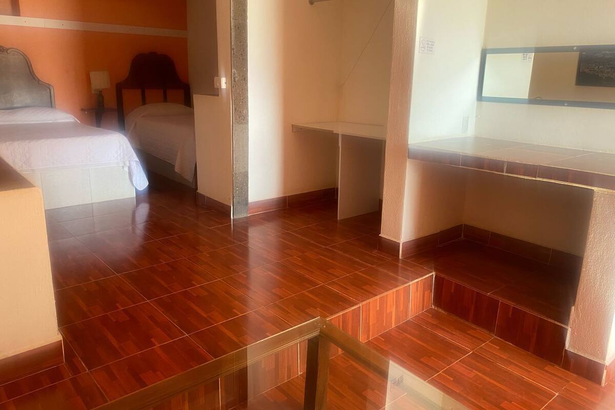A hotel room with a wooden floor, a bed, a desk, and a chair.