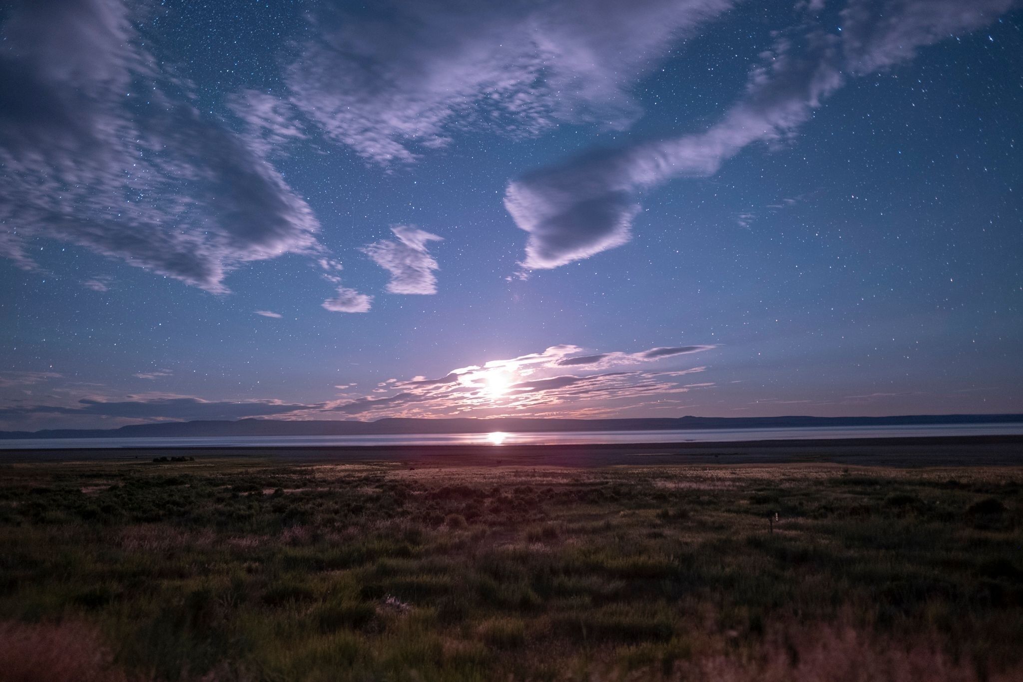 A starry night sky over a grassy landscape with a sunset.