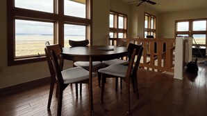 Ein Essbereich mit Tisch und Stühlen, große Fenster mit Blick auf den Strand und ein Deckenventilator.