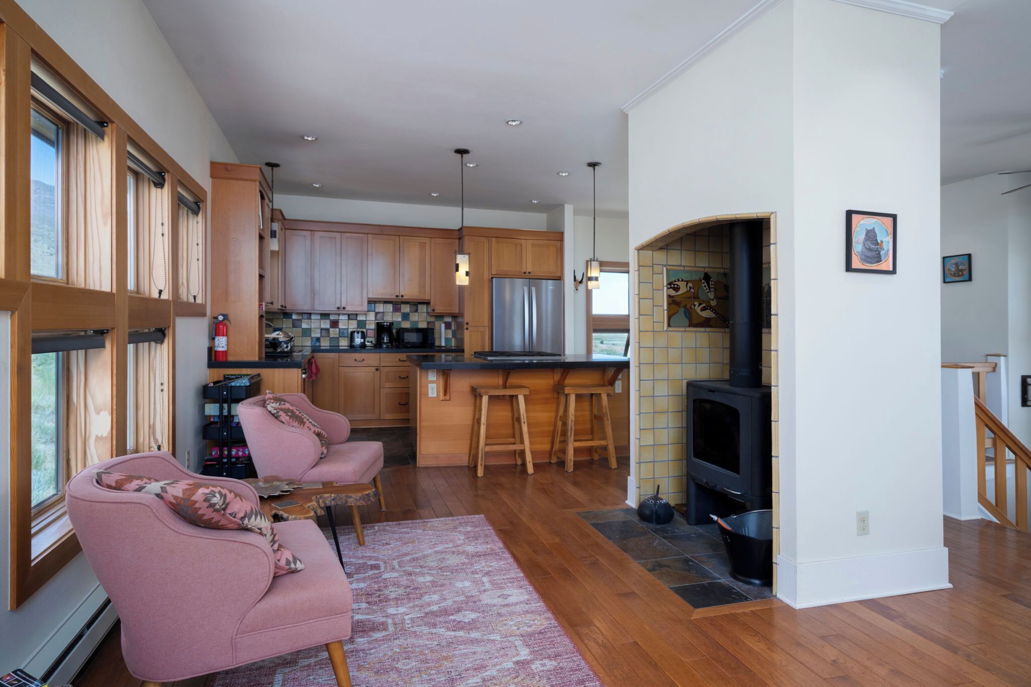 Una cocina moderna con armarios de madera, electrodomésticos de acero inoxidable y una estufa integrada. Hay una zona de estar con un sofá rosa y una alfombra.