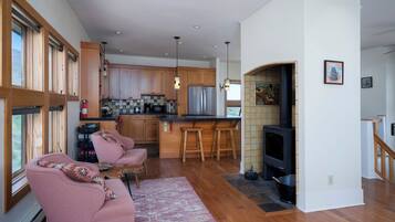 Una cocina moderna con armarios de madera, electrodomésticos de acero inoxidable y una estufa integrada. Hay una zona de estar con un sofá rosa y una alfombra.
