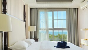 Une chambre d’hôtel avec un grand lit, deux lampes de chevet, une vue sur la mer et une fenêtre avec des rideaux.