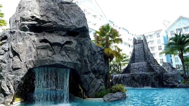 Une piscine d’un complexe hôtelier agrémentée d’une cascade, entourée de grandes formations rocheuses et de palmiers.