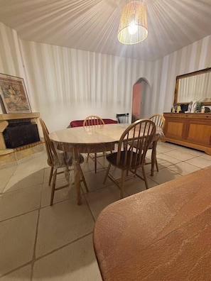 A dining area with a round table, wooden chairs, a chandelier, a fireplace, and a framed picture on the wall.