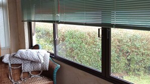 Quarto com móveis de vime, janela com persianas e vista para o verde lá fora.