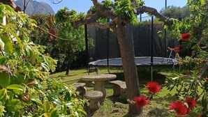 A garden with a stone table and chairs, surrounded by lush greenery and palm trees. - Villa with a pool near the Gulf of Lava in July and August  (Appietto)