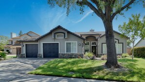 A two-story house with a garage, a stone foundation, and a well-maintained lawn. - Spacious 5-bedroom tropical paradise resort style pool spa scenic sunset views (Roseville)