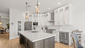 A modern kitchen with white cabinetry, a large island, stainless steel appliances, and pendant lighting. - Spacious 5-bedroom tropical paradise resort style pool spa scenic sunset views (Roseville)