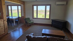 Un salón amplio con techo de madera, un sillón verde, un sofá de cuero, una mesa de centro de madera y vistas a un paisaje verde a través de grandes ventanales.