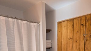 Un baño con cortina de ducha, armario de madera y estante con toallas dobladas.
