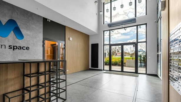 Un espace d’accueil moderne avec un mur en béton, un comptoir en bois et une grande porte vitrée donnant sur l’extérieur.