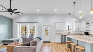 A modern kitchen with white cabinets, a central island with stools, and a ceiling fan. - Waterfront Escape in Bay STL with dock,pickleball, ping pong, basketball & more! (Bay St. Louis)