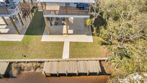 A modern houseboat with a deck and a small outdoor area, surrounded by natural vegetation. - Waterfront Escape in Bay STL with dock,pickleball, ping pong, basketball & more! (Bay St. Louis)