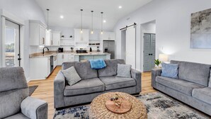 A modern living room with grey sofas, a coffee table, and a kitchen in the background. - Waterfront Escape in Bay STL with dock,pickleball, ping pong, basketball & more! (Bay St. Louis)