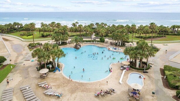 A resort with a large central pool surrounded by palm trees, a beach area with sun loungers, and a view of the ocean. - 502 Gorgeous 2 bdrm~ Private Beach ~ Gulf View & Pools ~ Book Sept 21st Special (Destin)