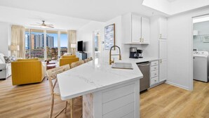 A modern hotel room with a large island kitchen, a dining area with yellow chairs, and a view of the cityscape. - 502 Gorgeous 2 bdrm~ Private Beach ~ Gulf View & Pools ~ Book Sept 21st Special (Destin)