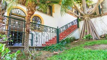 A staircase with ornate metal railings, a palm tree, and a building with a white facade and yellow trim.