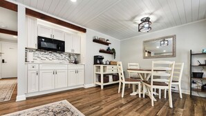 Una cocina moderna con armarios blancos, un microondas negro y un comedor con sillas de madera y una mesa.