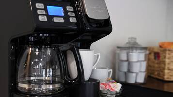 Une machine à café dotée d’un écran numérique, d’une verseuse en verre, d’une tasse blanche et d’un récipient contenant des capsules de café.