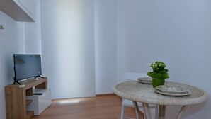 Ett stilrent, minimalistiskt rum med ett TV-bord i trä, ett runt bord av rotting med två tallrikar och en liten krukväxt, samt en vit stol.