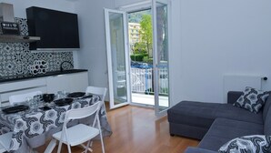 En modern lägenhet med ett matområde, en grå soffa och en balkong med utsikt över byggnader och träd.
