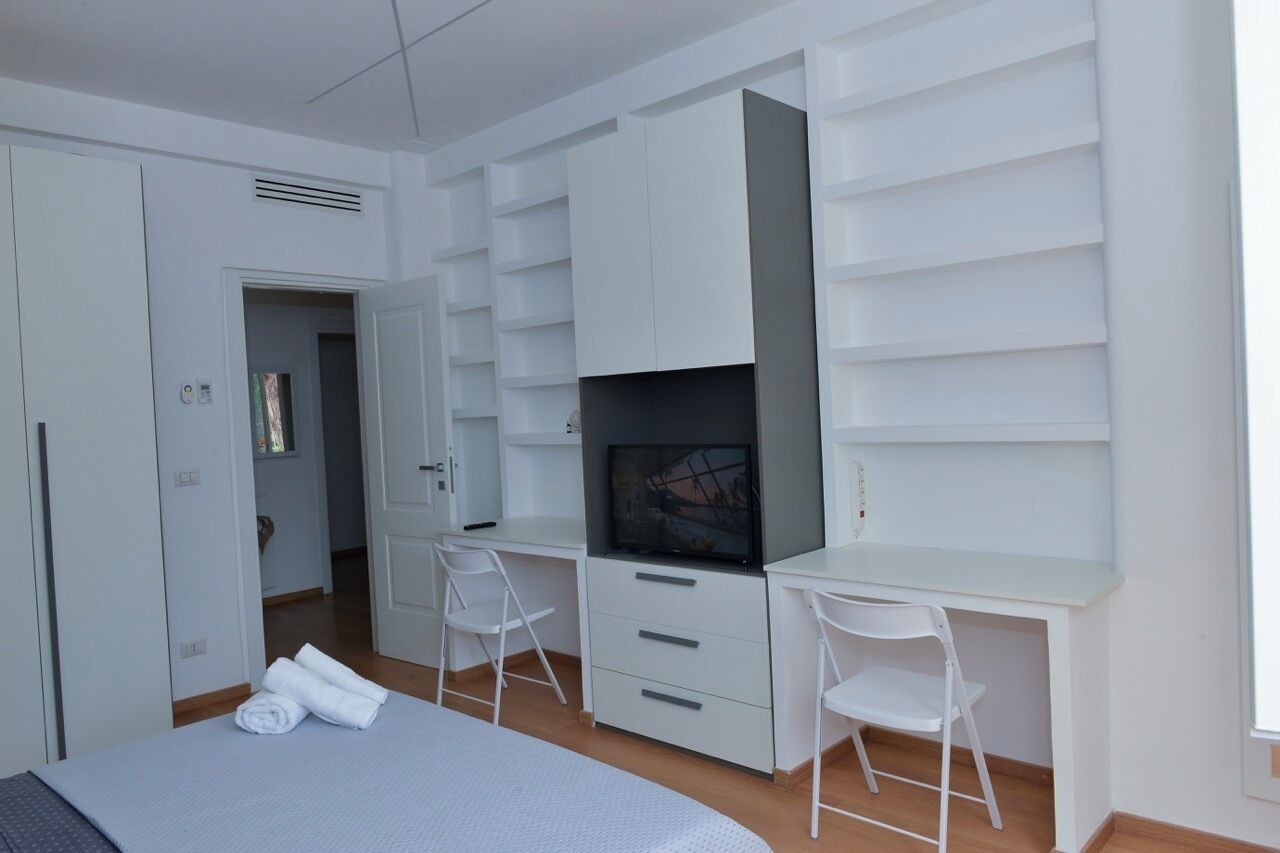 A modern bedroom with a bed, a desk, two chairs, and built-in shelving.