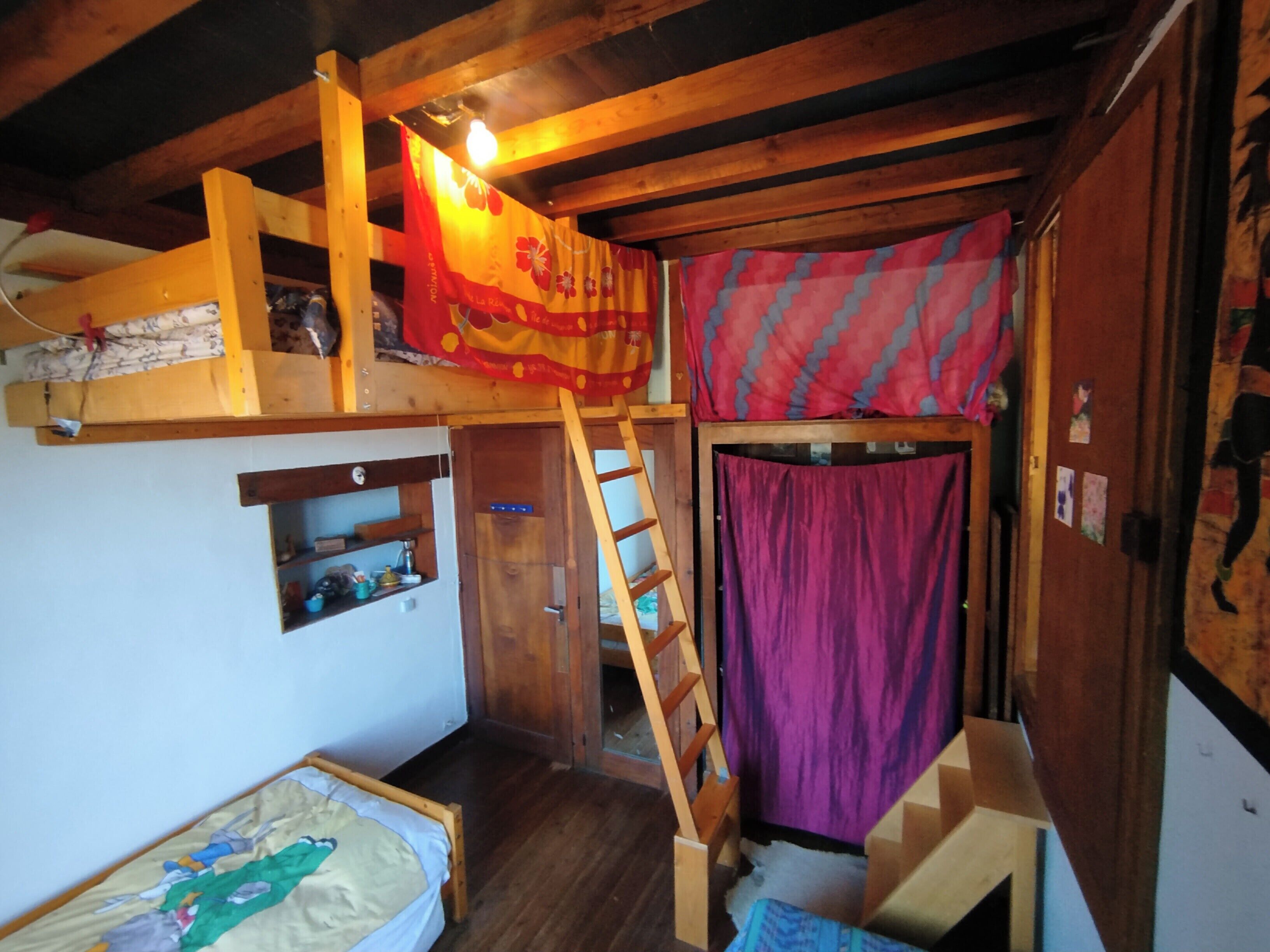 A compact room with a bunk bed, a ladder, a small shelf, and a door leading to another room.