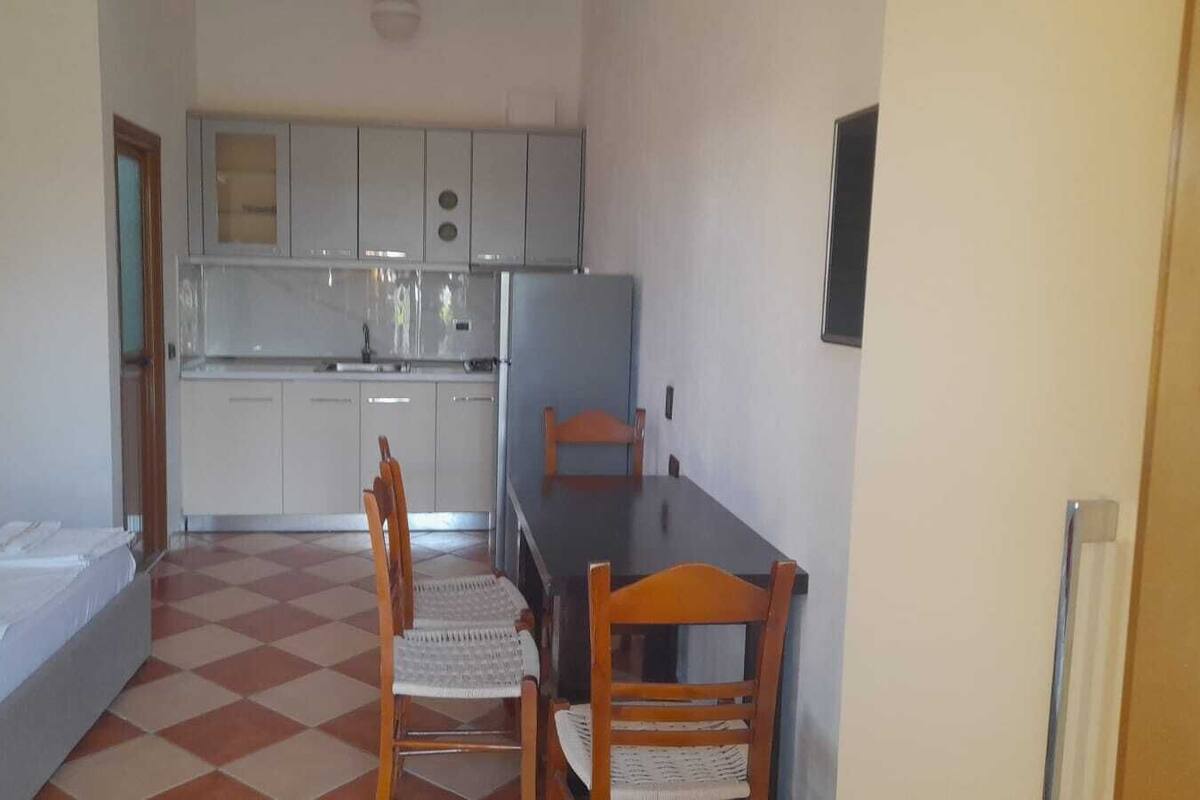 Una habitación compacta con cama, una mesita, dos sillas, kitchenette y un ventanal.