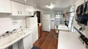 Une petite cuisine avec des meubles blancs, un réfrigérateur et un évier. Il y a un panneau sur le mur qui indique : « Faites la vaisselle ».